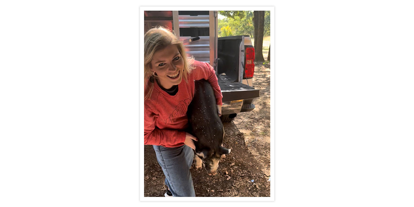 A woman wearing a red long-sleeve shirt holding a baby pig while getting it out of the truck.